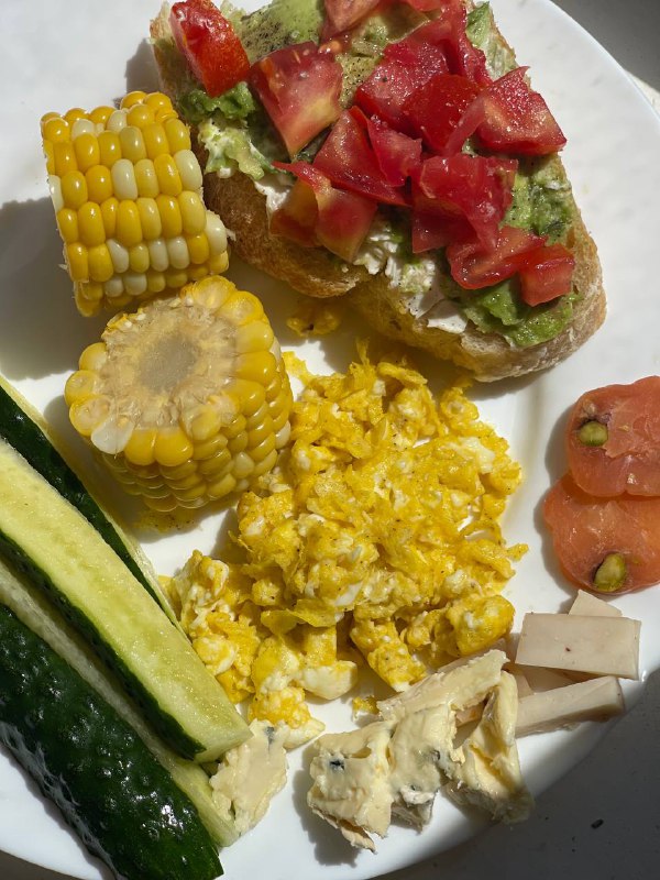 Mixed Plate With Avocado Toast, Scrambled Eggs, Corn On The Cob, And Vegetables